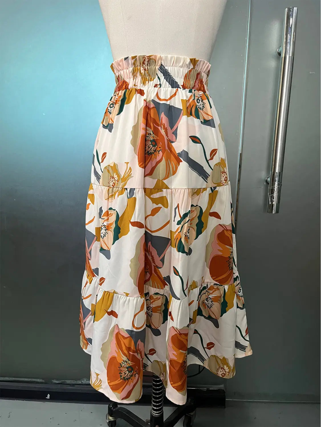 A cream tiered pleated floral print skirt featuring bold orange yellow and muted green blossoms on lightweight fabric with a floral print elastic waist.