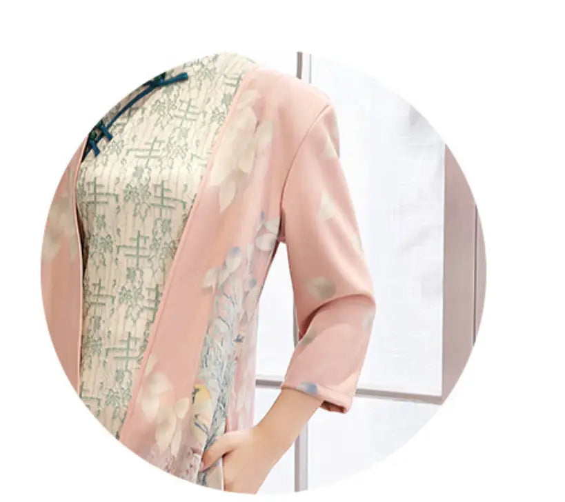 a medium length cheongsam floral dress set featuring a delicate pink sheer overlay jacket with floral patterns worn over a cream-colored dress with intricate green and beige embroidery