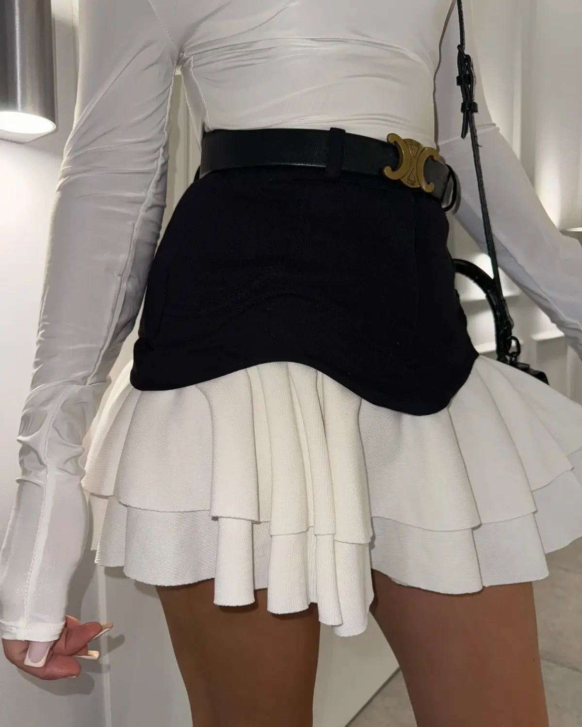 Black belted mini skirt with layered white ruffles and a gold-tone C-shaped buckle in a ruffled high waist tiered skirt design.