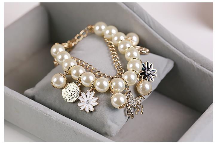 Navy pearl flower bracelet featuring a delicate gold-toned chain adorned with cream-colored pearls and dangling charms including a white flower, a black-and-white daisy, a silver coin pendant, and a small gold horse charm in flower bracelet jewelry design.