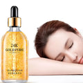 A clear glass bottle of 24k gold pure hyaluronic acid essence serum with gold-toned dropper cap and golden-yellow liquid