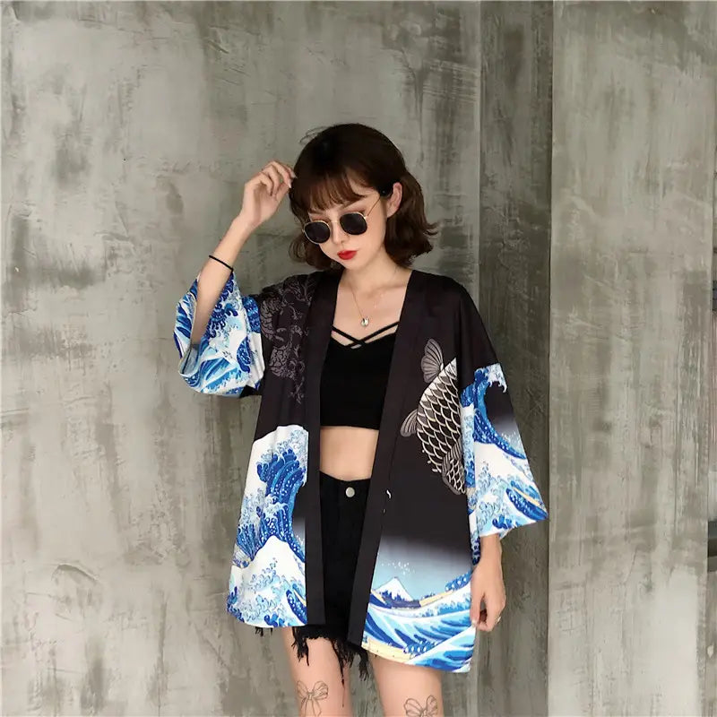 black kimono-style jacket with vibrant blue wave and fish prints featuring a flowing silhouette and frayed hem designed as sun protection clothing.