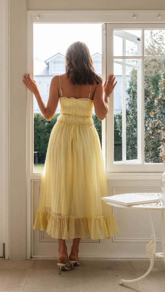 a flowing pale yellow summer suspender spaghetti strap lace midi dress with a fitted bodice and ruffled hem