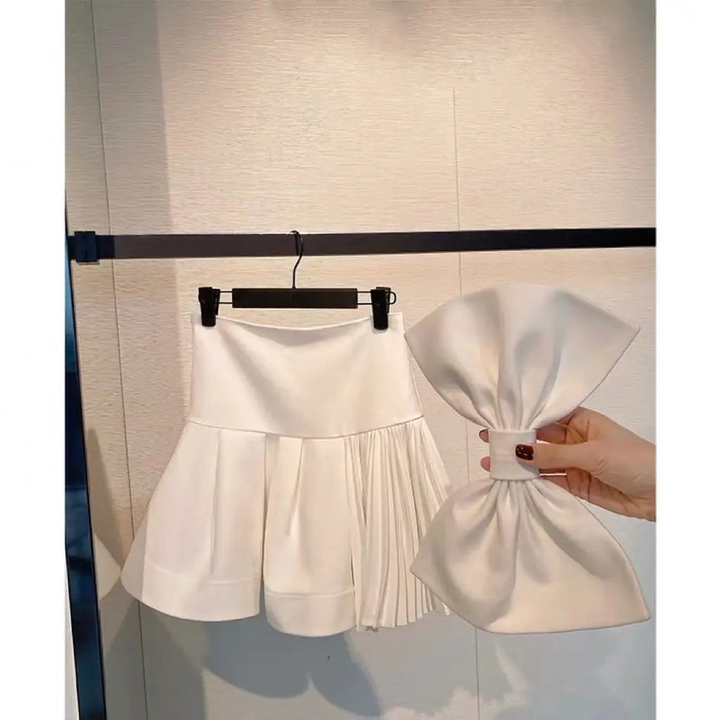 white high waist slimming pleated mini skirt with matching oversized bow accessory in lightweight fabric
