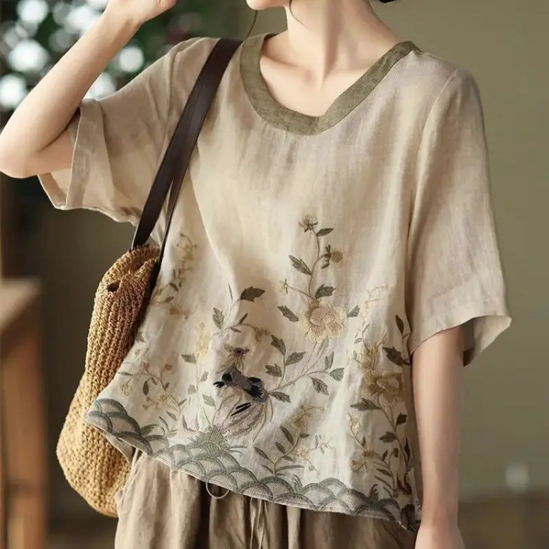 Beige linen round neck top with art retro embroidery of delicate floral and birds in earthy tones and a colored round neck and hem in olive green.