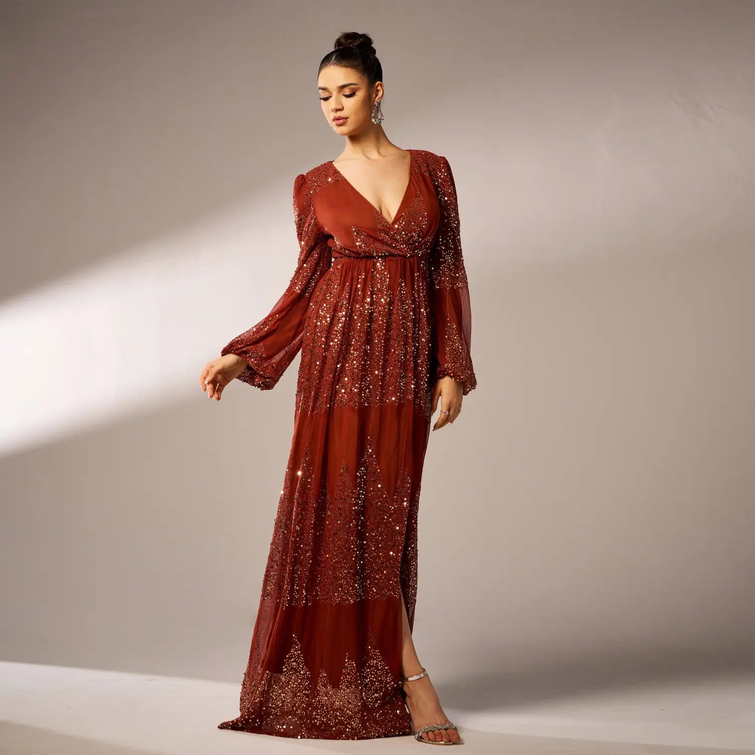 A rust-colored sexy long sequined evening dress with long sheer bell sleeves and a deep v-neckline featuring cascading sparkling sequins on the bodice and skirt.