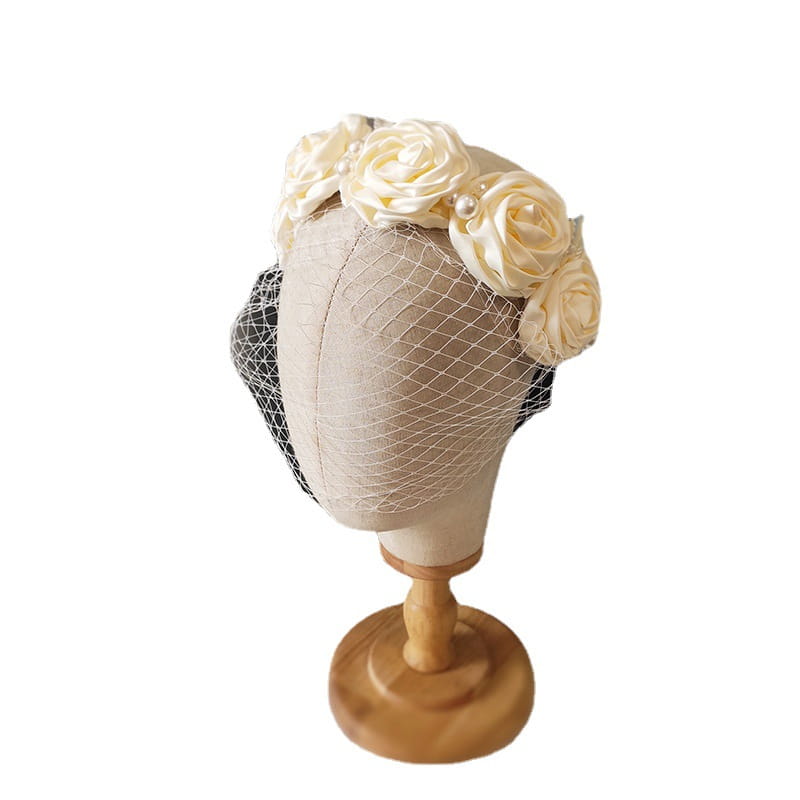 Elegant ivory satin rose hair hoop headdress adorned with pearls and a delicate black mesh veil for wedding dress styling.