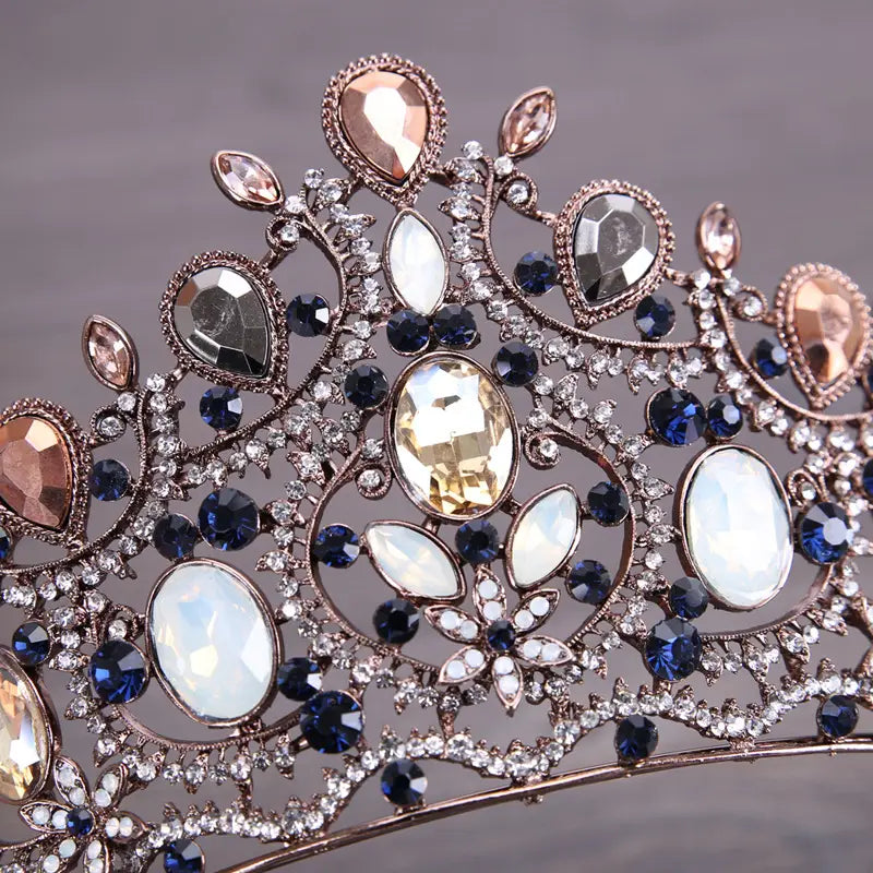 An ornate vintage elegant sapphire and diamond bridal crown tiara featuring a rose gold metal frame with deep blue and clear crystals accented by pear-shaped peach-toned stones.