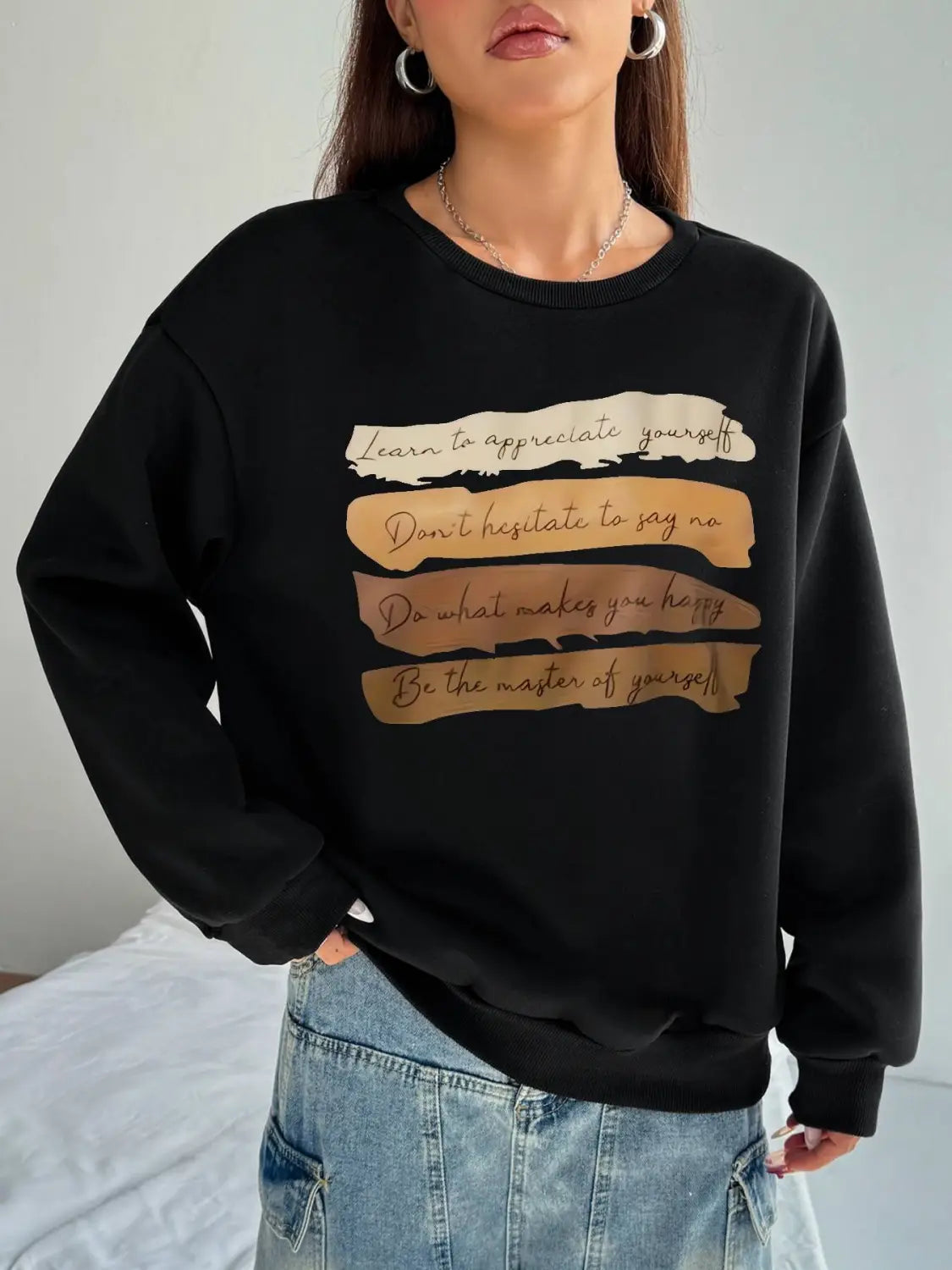 black oversized long sleeve sweatshirt with a motivational quote printed in gold foil on horizontal beige and tan strips designed for daily wear solid colour style.