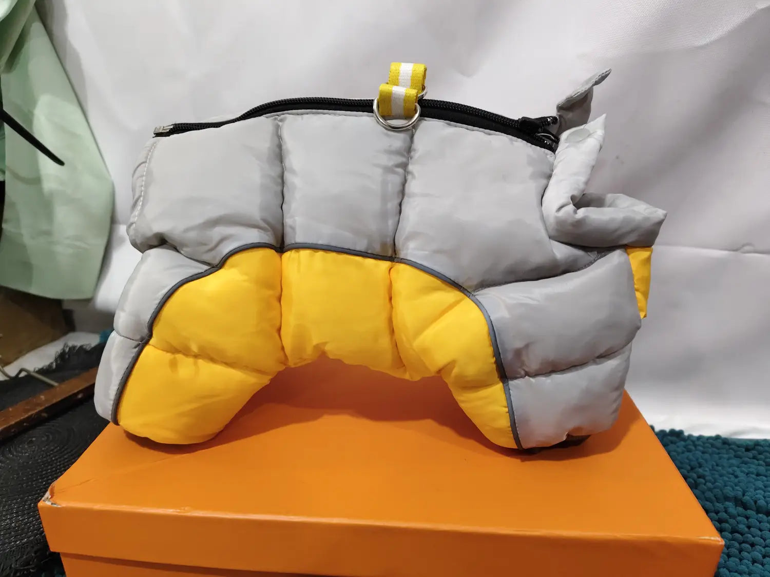 quilted orange and white pet dog winter clothes featuring a gray and yellow puffer design with a black zipper and a yellow-and-white striped strap for pet dog winter protection.