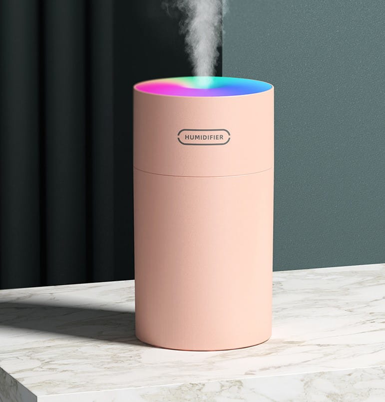 A sleek cylindrical pink second generation colorful cup humidifier with a rainbow-colored led ring at the top emitting mist and usb powered.