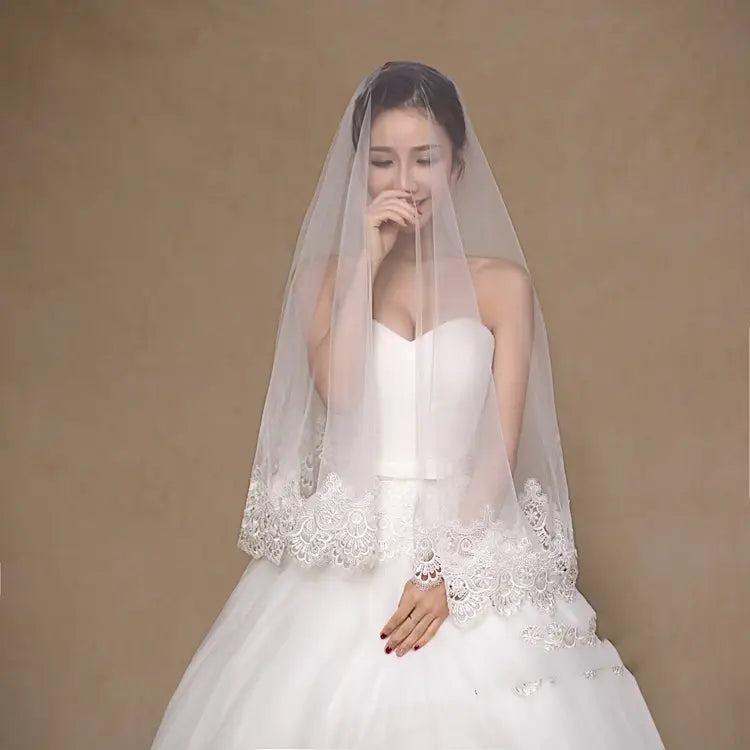 A delicate white lace white bride veil with intricate floral embroidery along the hem for a wholesale white bride looking for a bride veil cheap option.