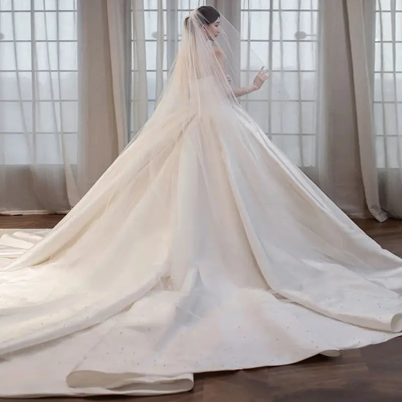 a flowing ivory wedding veil with delicate beading along the hem gracefully draped over the back of a bride wearing a temperament princess style french satin wedding gown