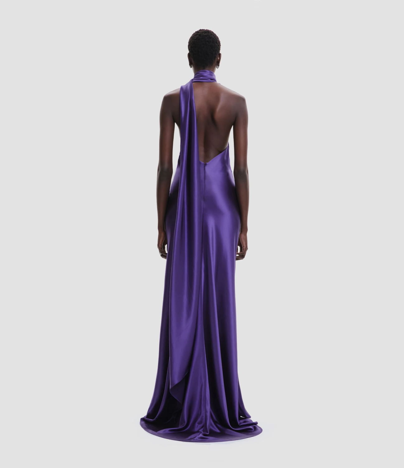 a flowing deep purple satin gown with a fitted high waist featuring a halter neckline and an open back view