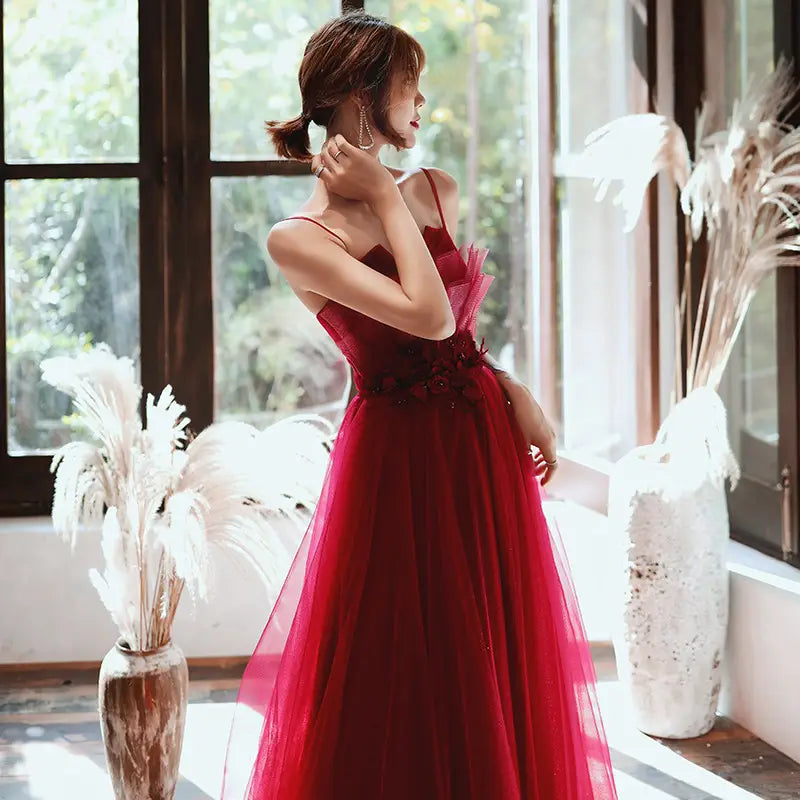 a flowing red satin evening dress with a fitted bodice featuring floral embellishments and thin spaghetti straps designed for engagement suspender wear engagement suspender evening occasions