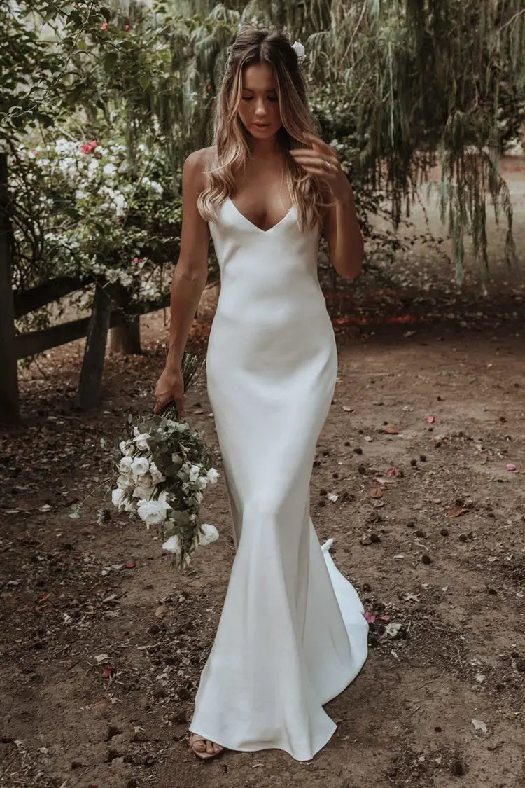 A sleek white satin evening gown with a mermaid silhouette deep v neckline and subtle side slit shown in a train brigade shot.