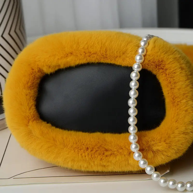 A yellow checkerboard plush bucket bag featuring mustard-yellow faux fur, black leather interior, and a pearl chain design strap.