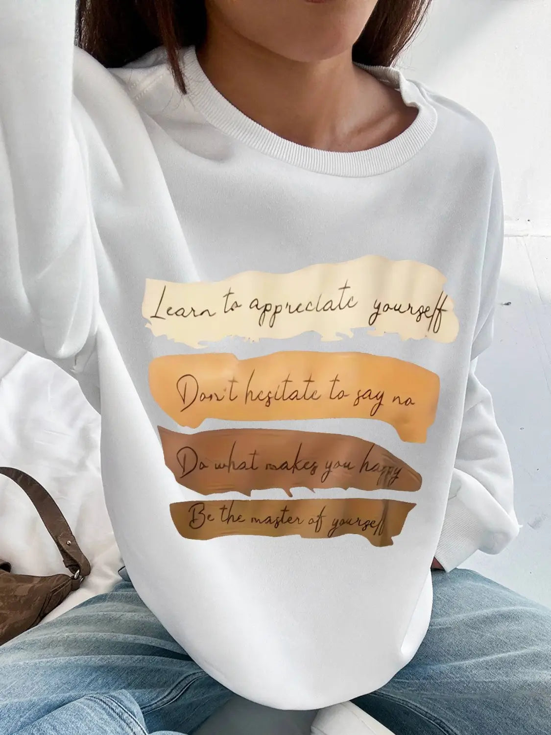 White oversized long sleeve sweatshirt in solid color with a layered torn-paper design and motivational phrases in brown and gold script on beige and tan stripes ideal for daily wear.