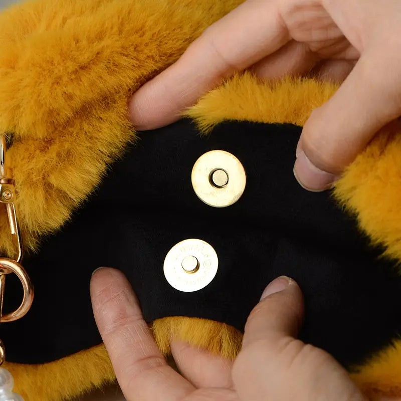 Gold-toned magnetic snap buttons on the black and yellow checkerboard plush bucket bag with pearl chain design.