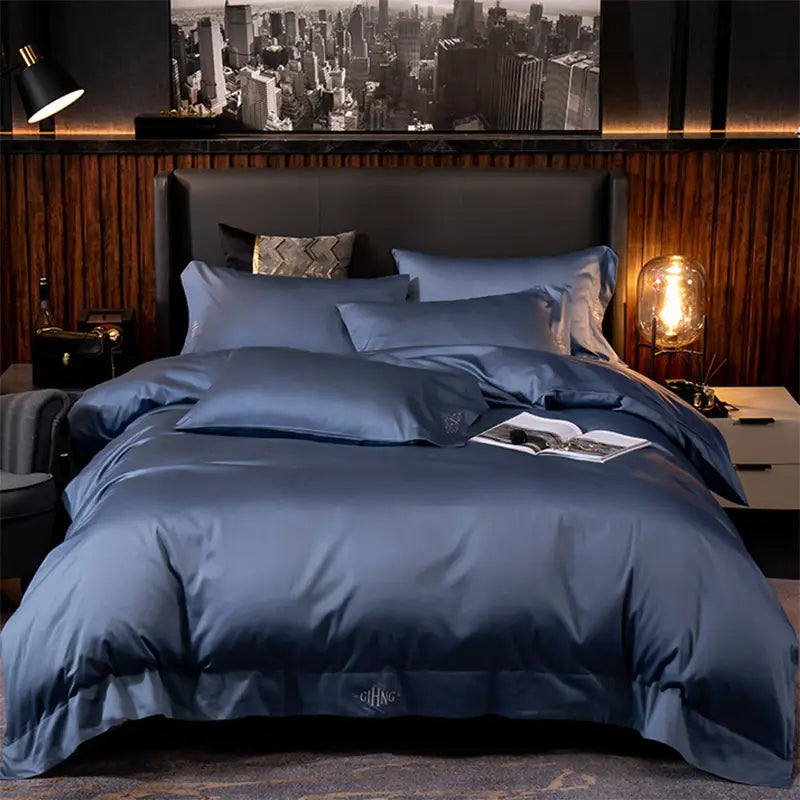 purple satin embroidered four-piece bed sheet set featuring deep blue satin bedding with a subtle embroidered logo at the foot of the duvet
