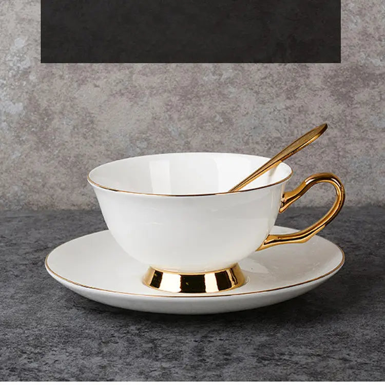 White porcelain bone china coffee cup with gold trim and matching saucer afternoon tea set featuring a golden spoon inside the cup.