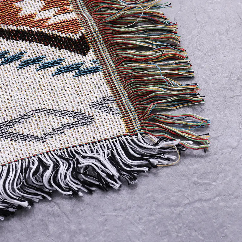 A geometric woven sofa blanket sofa in earthy tones and black with multicolored fringes along the edges designed as a blanket sofa towel.