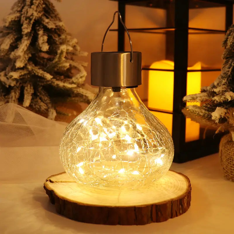 a warm glowing solar crackle glass small night light with fairy lights inside sits on a rustic wooden slice providing a night light ambient glow