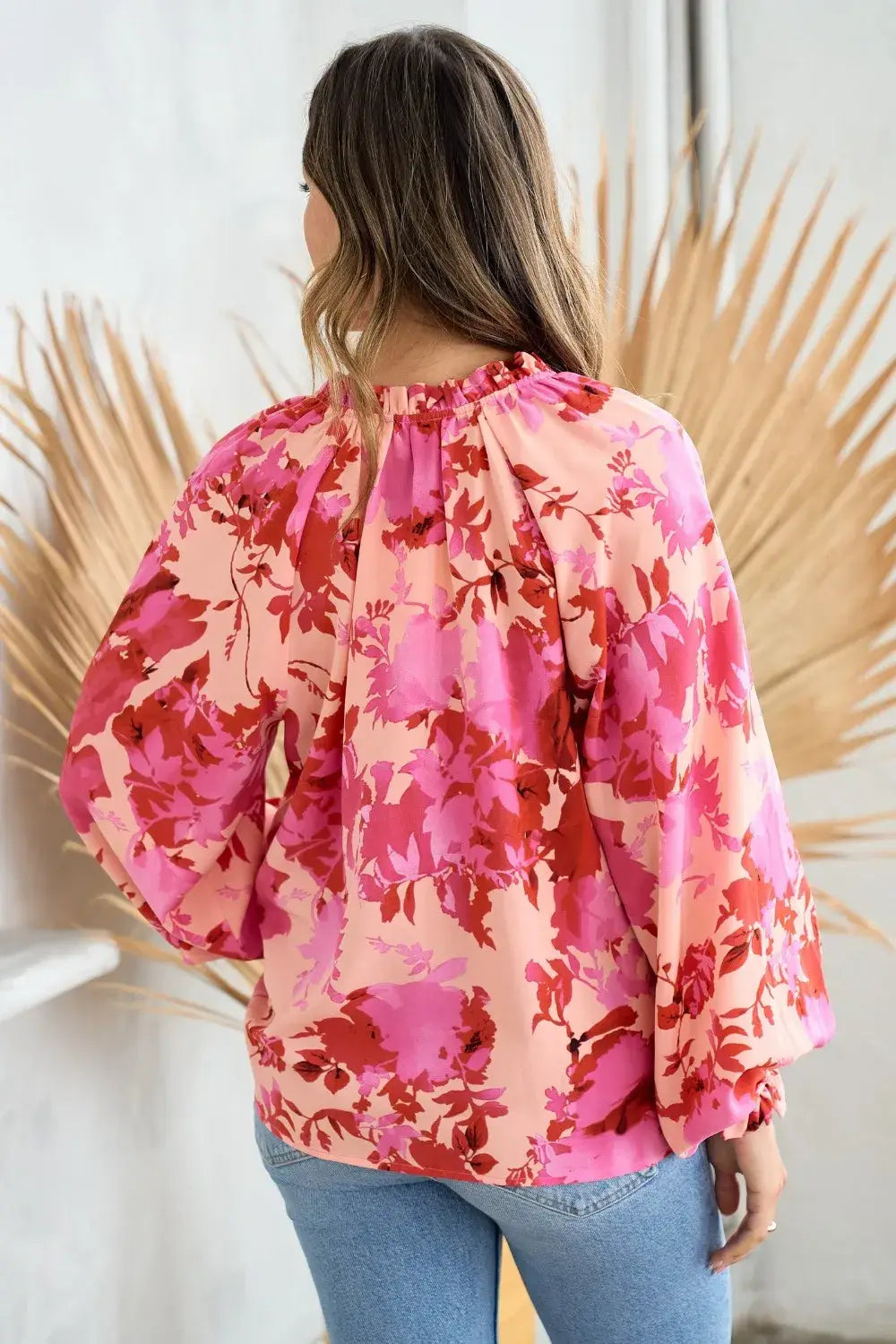 A woman wears a pink and red decor button floral blouse featuring puffy sleeves and a floral print design.