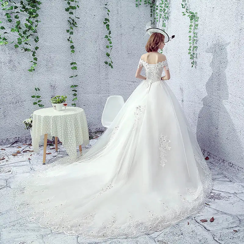 A flowing white wedding dress bride featuring delicate lace detailing and off-the-shoulder sleeves paired with a trailing french veil.