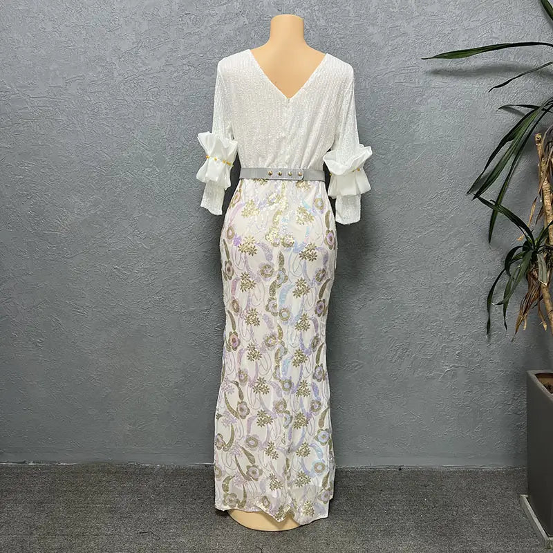 A white half sleeve slim fit maxi dress with a round neck shirt design featuring a v-neckline and ruffled cuffs with an intricate floral pattern in soft gold and lavender hues across the skirt.