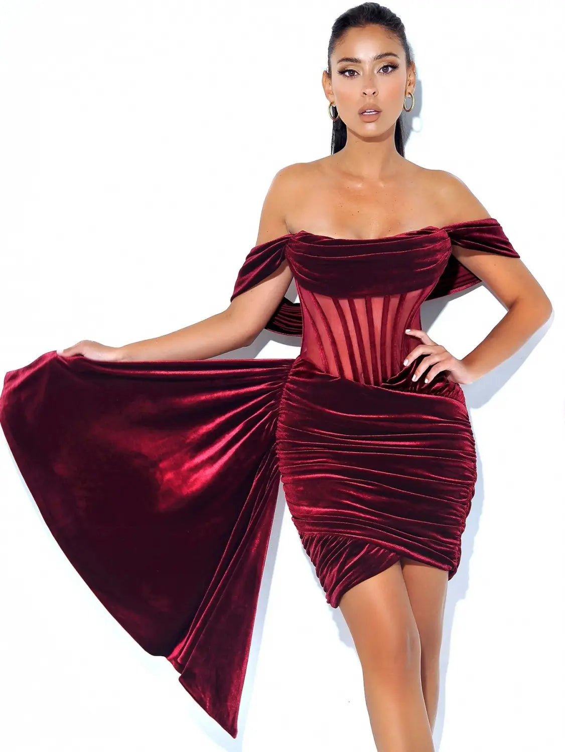 A form-fitting off the shoulder burgundy velvet dress with a corseted bodice and flowing side panels ideal as a breast sexy evening dress.