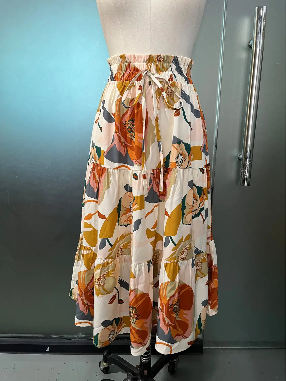 a cream tiered midi skirt featuring a pleated floral print in orange and mustard tones with a floral print elastic drawstring waistband