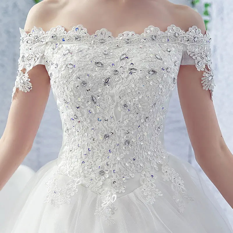 white off-the-shoulder wedding dress bride adorned with intricate lace and sparkling rhinestones paired with a trailing french veil