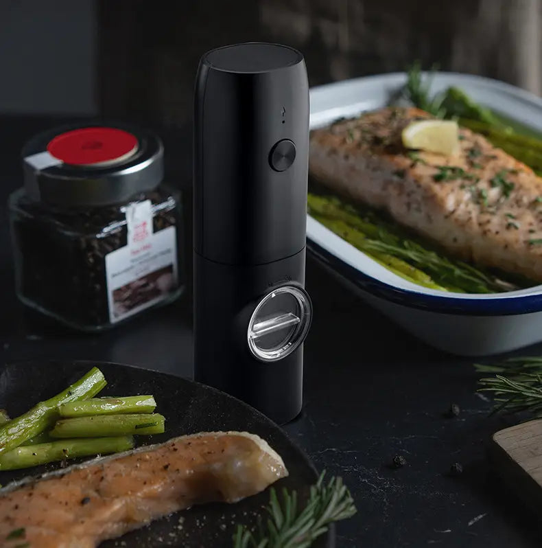 black cylindrical electric kitchen household pepper mill with a silver-toned circular dial and control button for grinding spices in a kitchen household grinder set