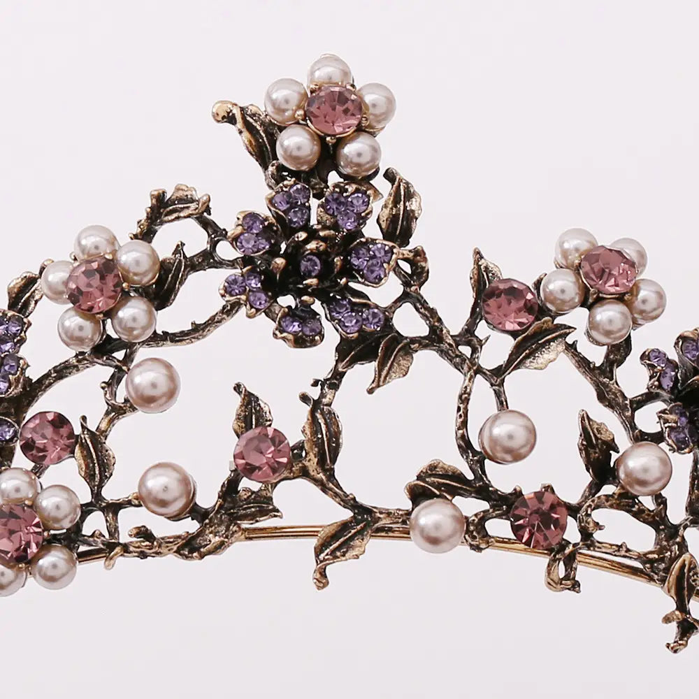 An ornate floral black diamond pearl baroque bridal crown with intricate metalwork featuring clusters of pink and purple crystals accented by round white pearls.