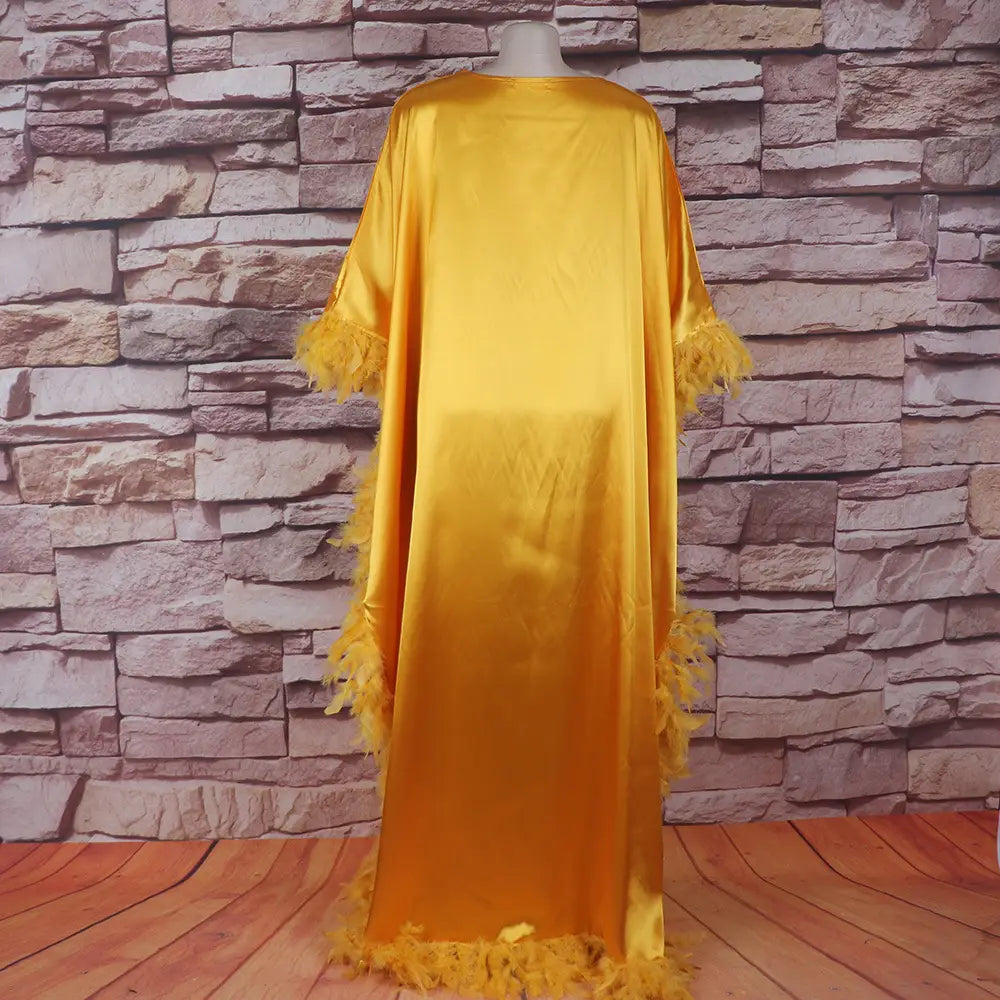 A flowing golden satin orange feathered loose dress luxury robe featuring feather trim along the sleeves and hem.