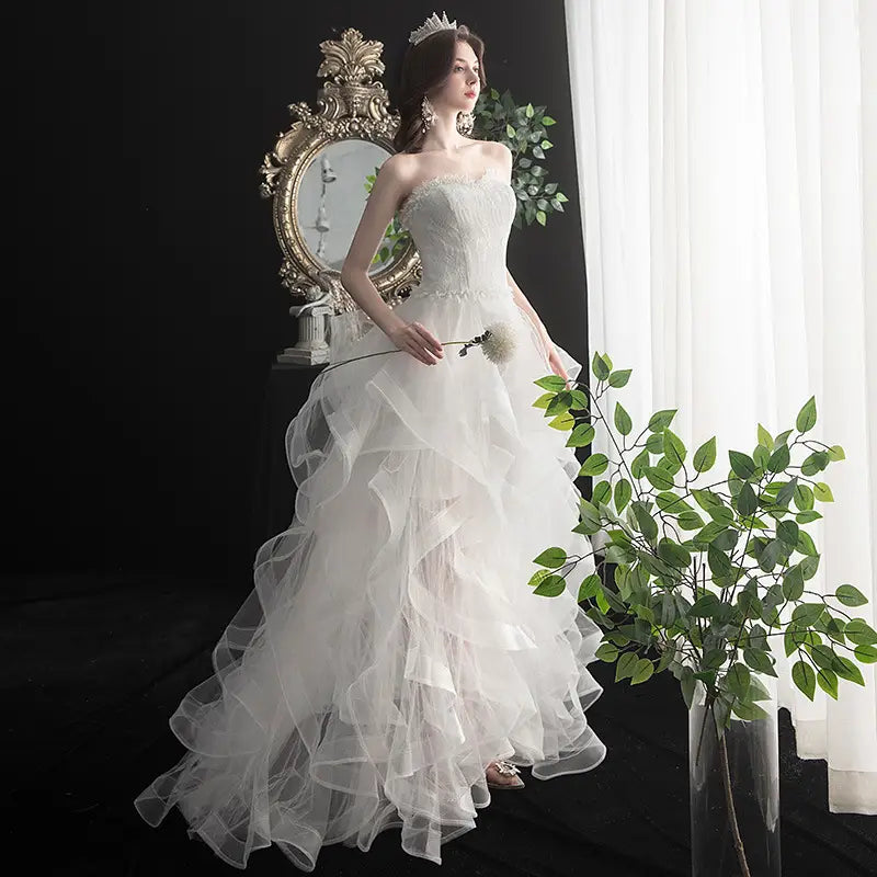 a strapless white small trailing wedding dress featuring intricate lace detailing on the bodice and a voluminous layered tulle skirt length small trailing