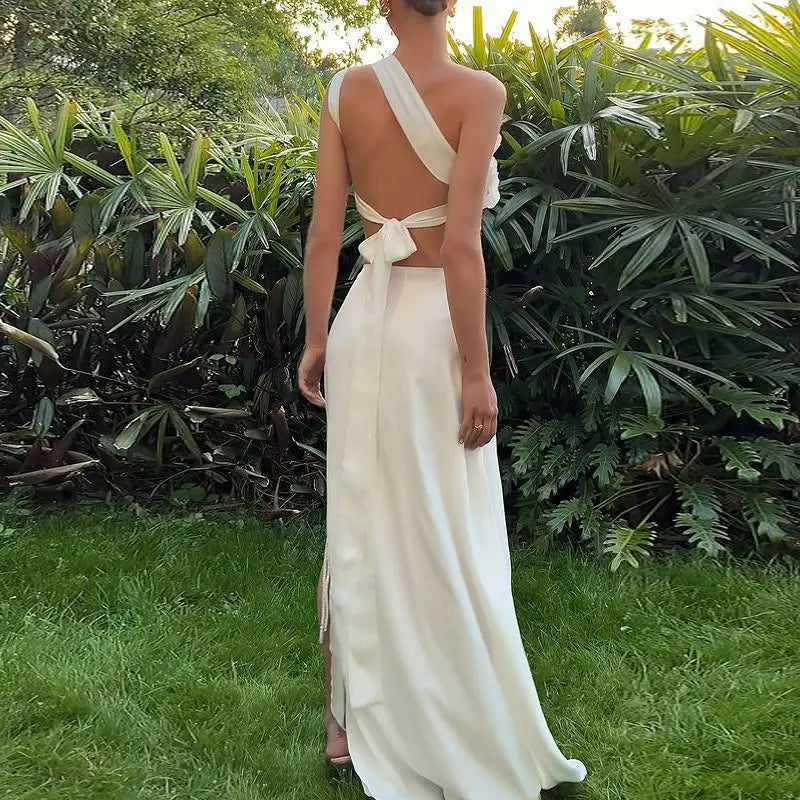 A flowing off-white satin maxi dress with a one-shoulder design and a tied bow at the back, complementing the backless sequined lace split skirt suit.