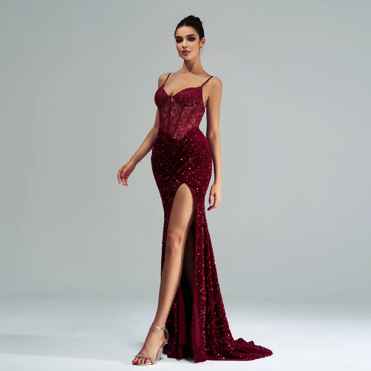 A burgundy sleeveless sequined high slit evening dress featuring a shimmering mermaid gown silhouette with a lace bodice and spaghetti straps.