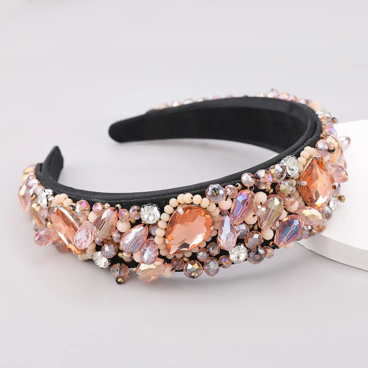 A glamorous black crystal geometric glass drill headband adorned with peach, rose gold, and clear faceted crystals and delicate cream-colored beads.