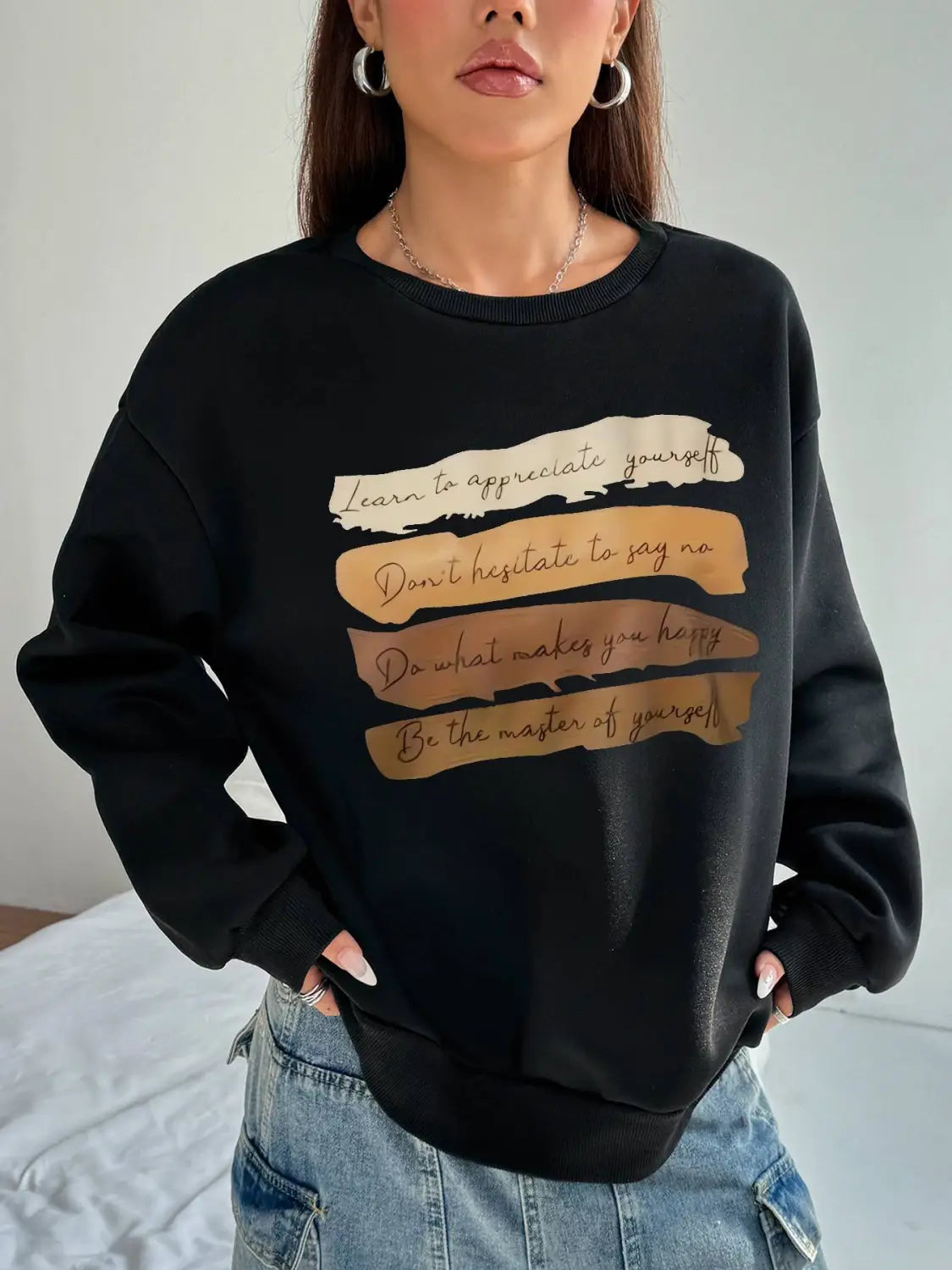 Black oversized long sleeve sweatshirt with a motivational quote printed in gold and cream brushstroke designs across the chest ideal for solid colour daily wear.