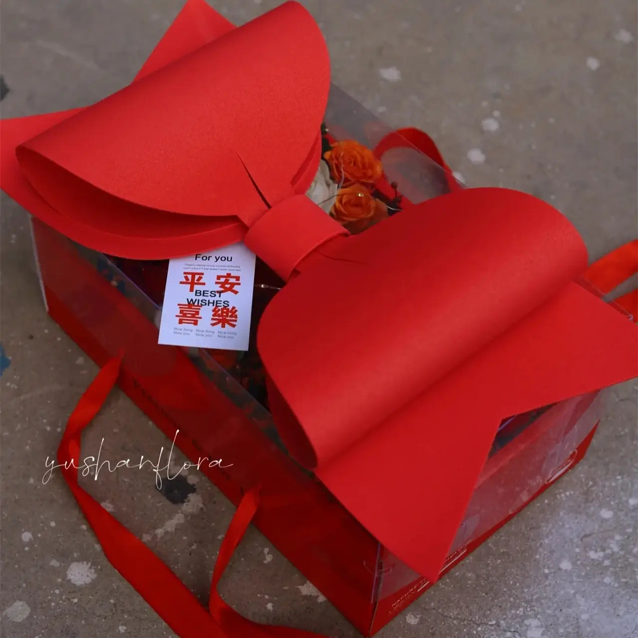 A vibrant red bow knot handheld adorns a transparent handheld flower box with a clear window.