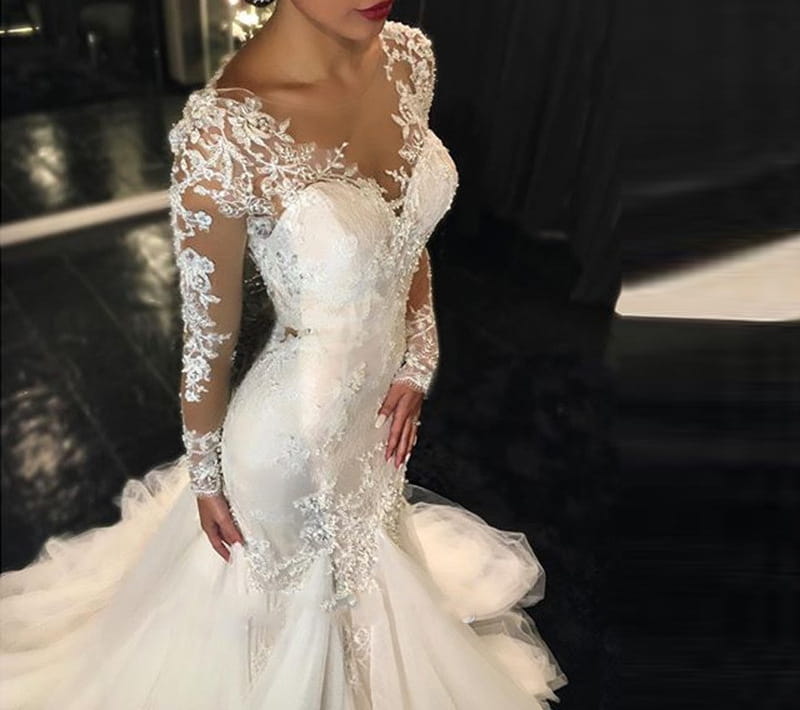 A white trailing white temperament long lace wedding dress made of polyester fiber with intricate lace detailing and long sheer sleeves.