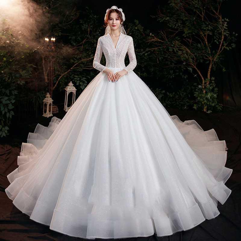A white long-sleeved ball gown featuring intricate lace detailing on the bodice and a voluminous tulle skirt embodying elegant bridal temperament trailing with trailing long sleeves.