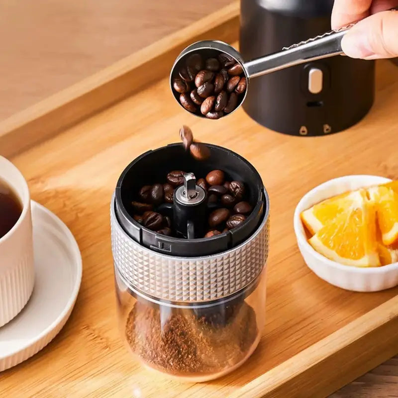 A sleek transparent glass portable electric ceramic coffee grinder with a textured silver metallic top and black components featuring USB charging.