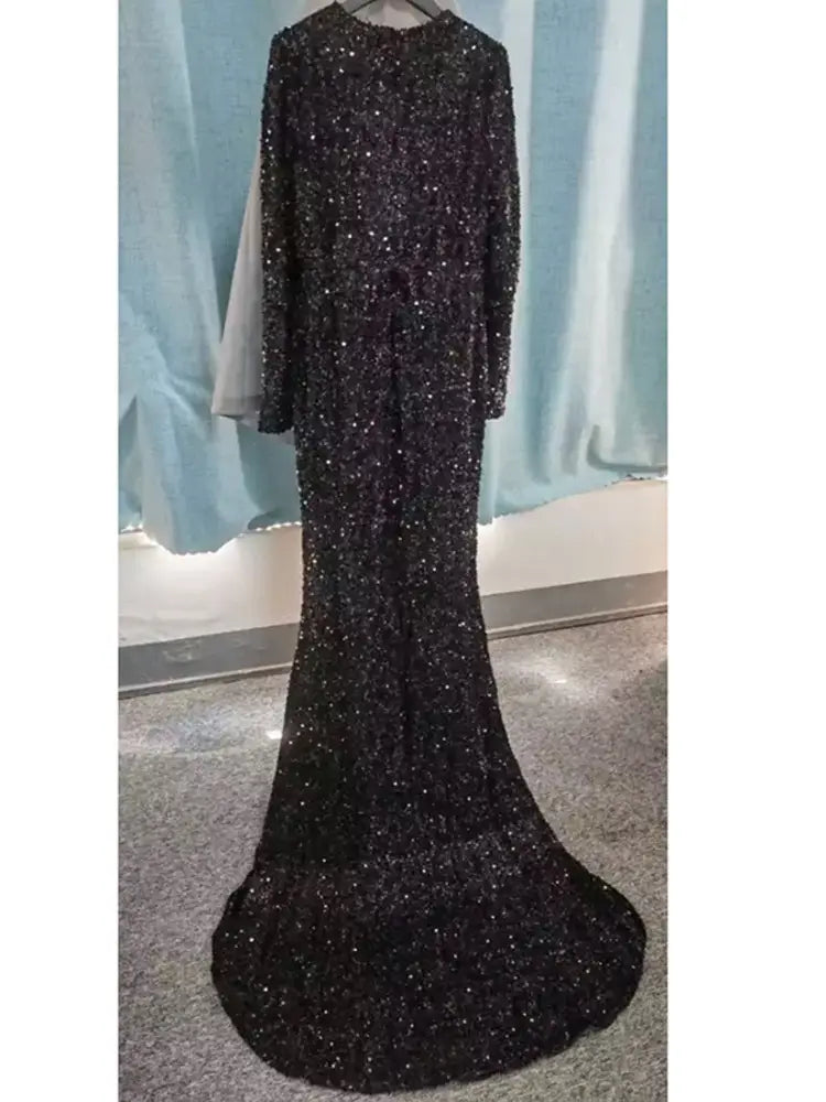 A grey long sleeve evening dress featuring a black sequined mermaid-style gown with long sleeves and a sheer overlay designed as a long sleeve sequin evening dress.
