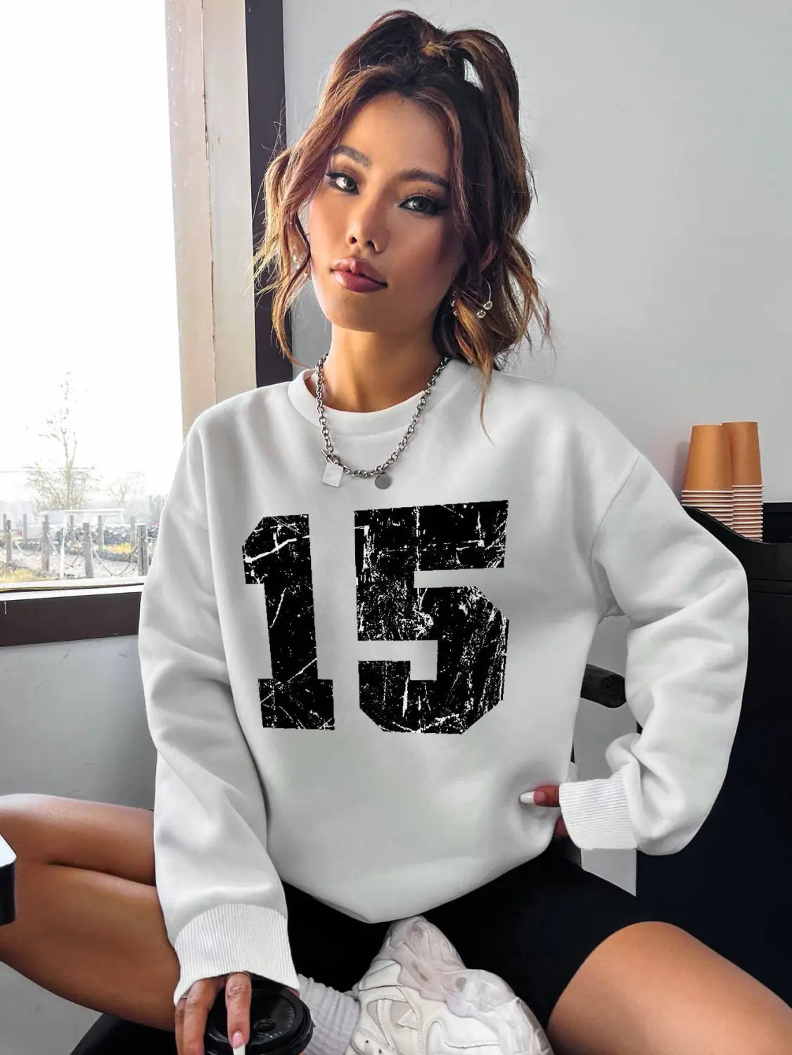 white crew neck sweatshirt featuring a black distressed number 15 graphic on the front.