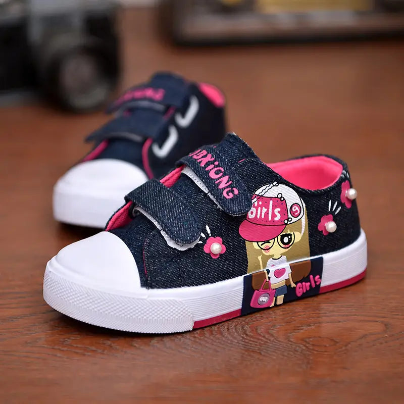 blue denim girls canvas shoes featuring navy blue canvas, pink velcro straps, white rubber toe caps and soles with red trim, and a cartoon girl design on the side.