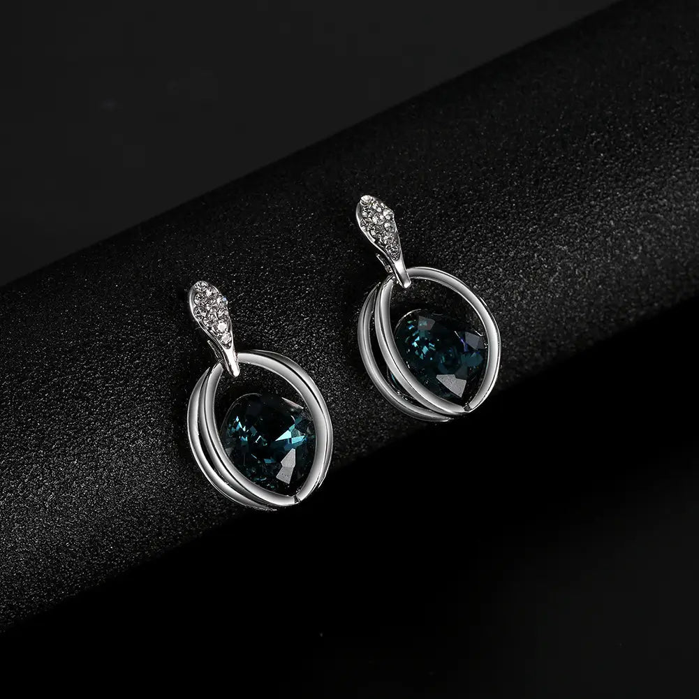 Elegant silver hoop earrings with a central deep blue gemstone and a diamond-encrusted leaf-shaped top complement a crystal bridal necklace featuring fashion inlaid crystal details.