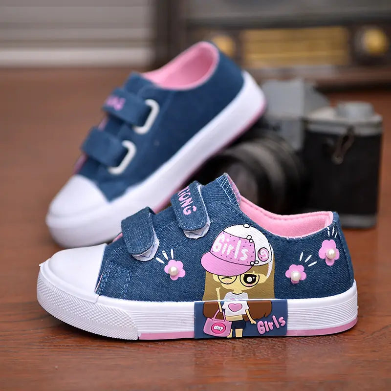 Blue denim girls canvas shoes with pink velcro straps white rubber soles and a cartoon girl design wearing a pink hat with floral accents.